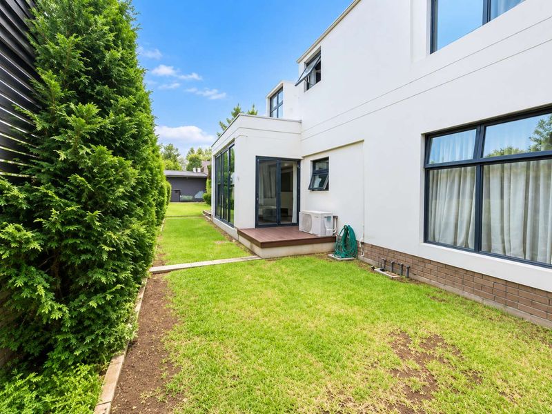 Rear exterior view of the townhouse featuring a small timber deck, manicured lawn, and modern white facade with large glass sliding doors.