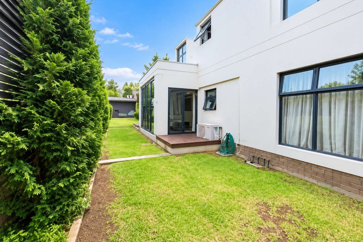 Rear exterior view of the townhouse featuring a small timber deck, manicured lawn, and modern white facade with large glass sliding doors.