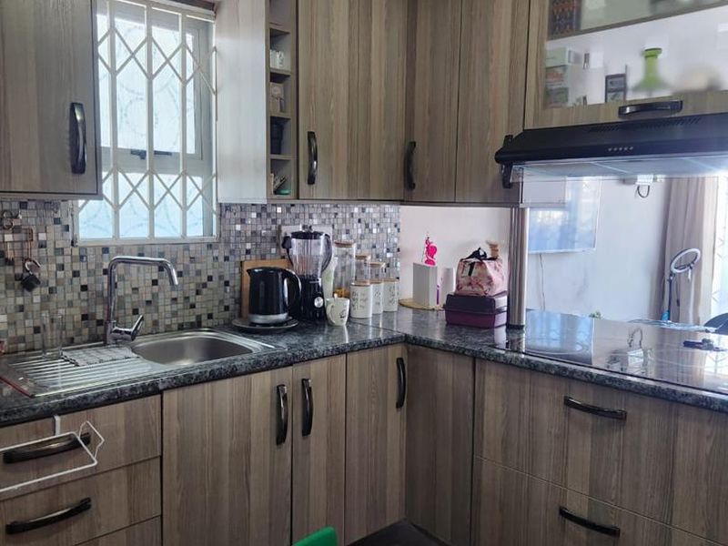 A functional kitchen featuring wood-look laminate cabinetry, granite countertops, a mosaic tile backsplash, and integrated appliances including a hob and extractor fan.