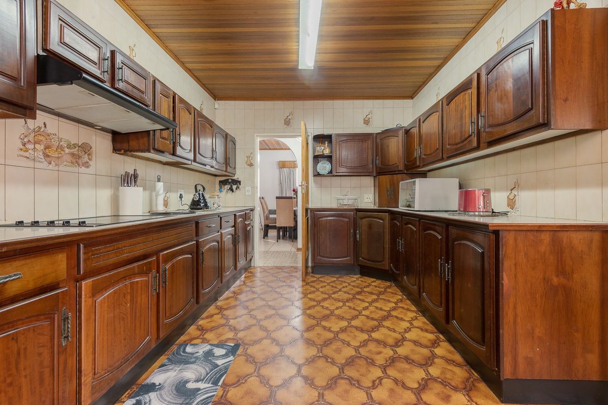 A traditional galley-style kitchen featuring extensive dark wood cabinetry, tiled backsplash, and a wooden ceiling, offering a classic layout with potential for modernization.