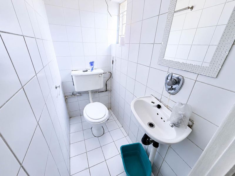 A compact, tiled guest bathroom featuring a pedestal basin and toilet, requiring minor cosmetic updates to improve its overall condition.