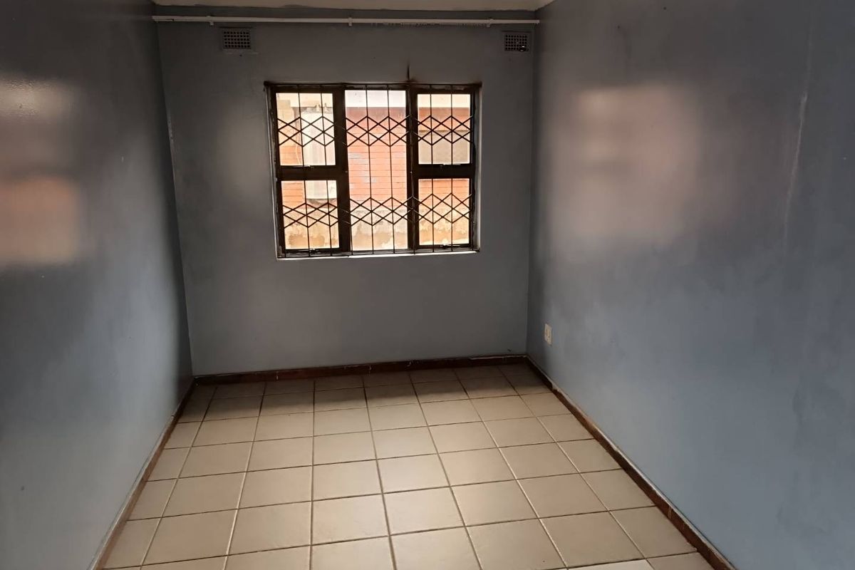 A vacant bedroom featuring tiled flooring, blue painted walls, and a window fitted with security bars.