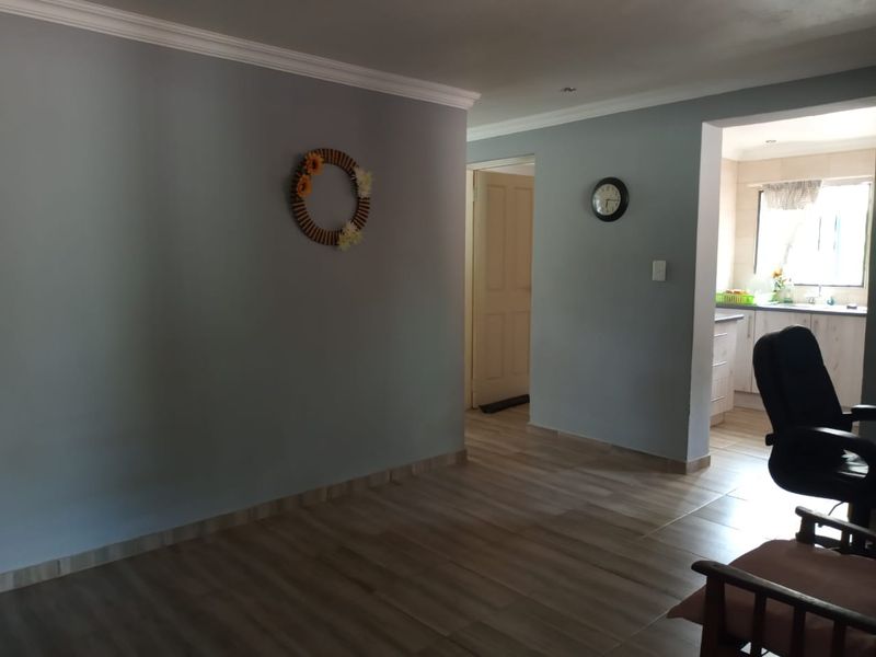 Open plan living area featuring wood-look tile flooring and crown molding, with a view through to the kitchen area.