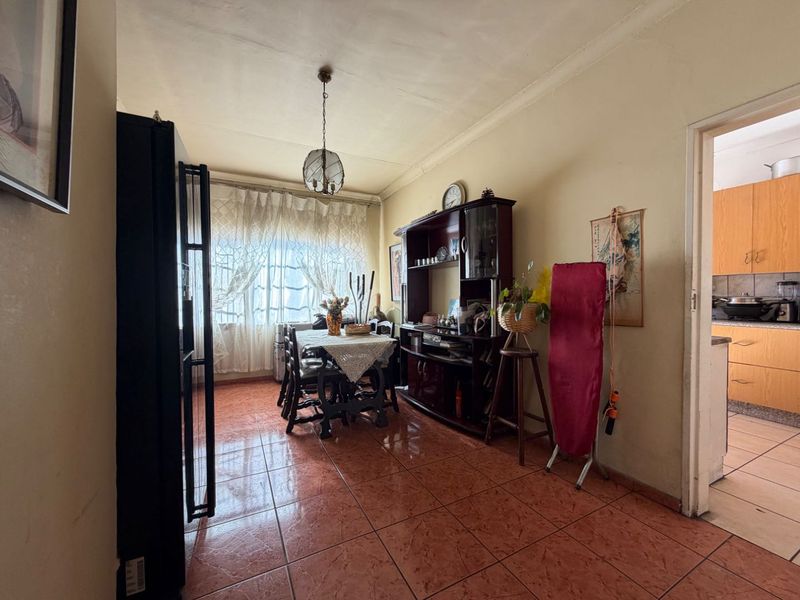A dining area featuring tiled flooring and a pendant light fixture, with a view into the adjacent kitchen.