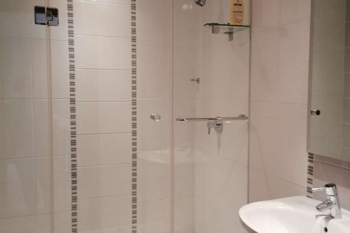 A clean, modern bathroom featuring a glass-enclosed shower, pedestal basin with chrome fixtures, and neutral wall and floor tiling.