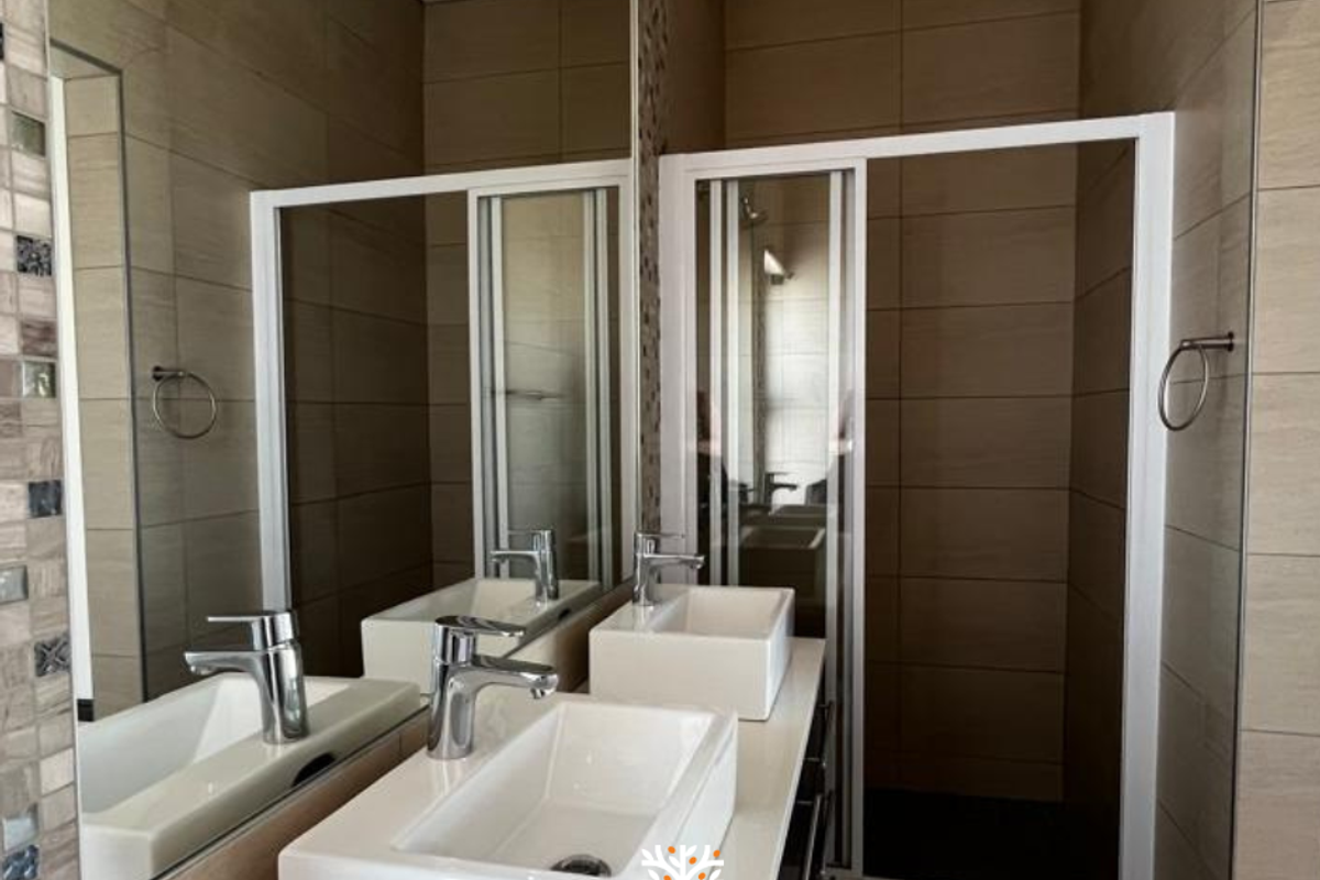 Modern bathroom featuring a double vanity with vessel sinks, large wall-mounted mirror, and a glass-enclosed shower with neutral wall tiling.