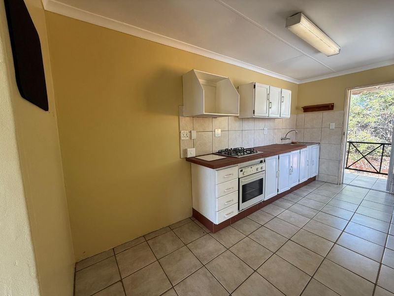 A functional kitchen featuring built-in cabinetry, a gas hob, an oven, and tiled flooring, with direct access to an outdoor area.
