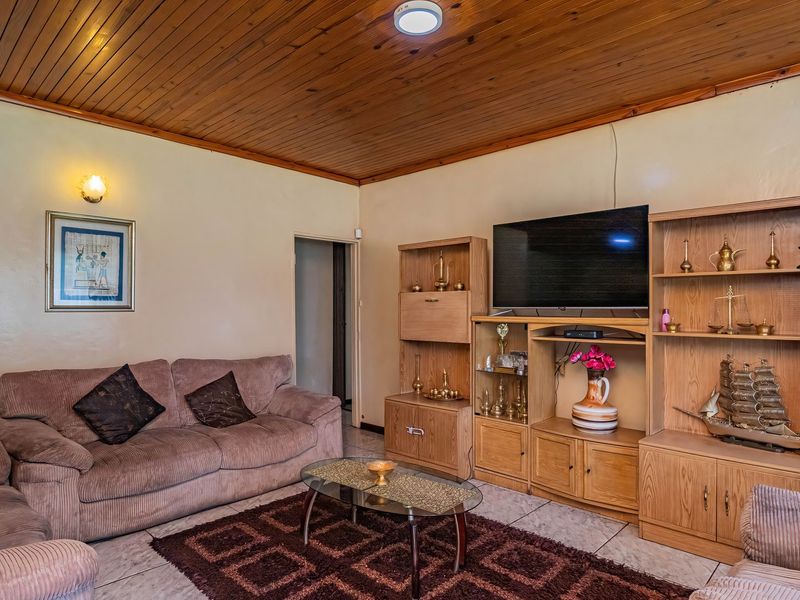 A living room featuring a timber tongue and groove ceiling, ceramic floor tiles, and a large built-in wooden wall unit.