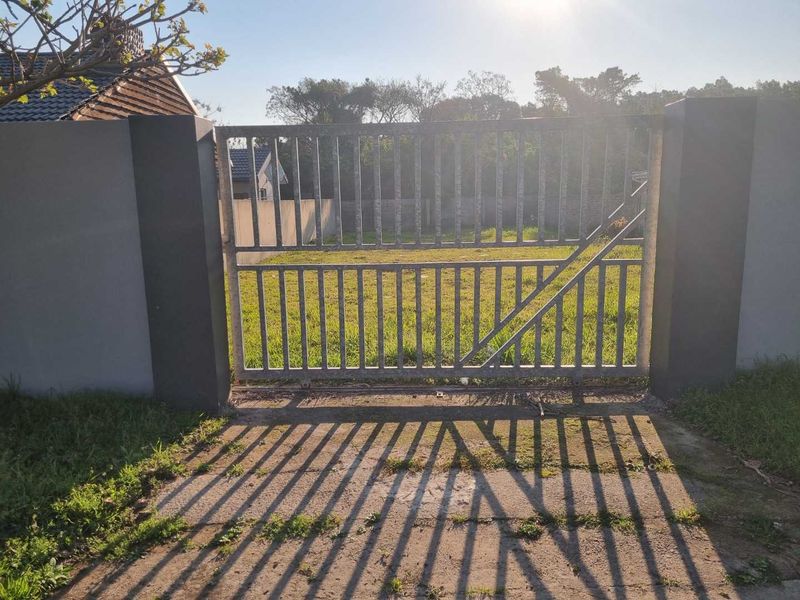 A front view of the property featuring a metal sliding gate, concrete driveway, and perimeter wall enclosing the front yard area.