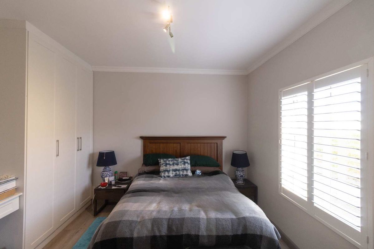 A well-maintained bedroom featuring built-in floor-to-ceiling wardrobes and plantation shutters on the window, providing a clean and functional living space.