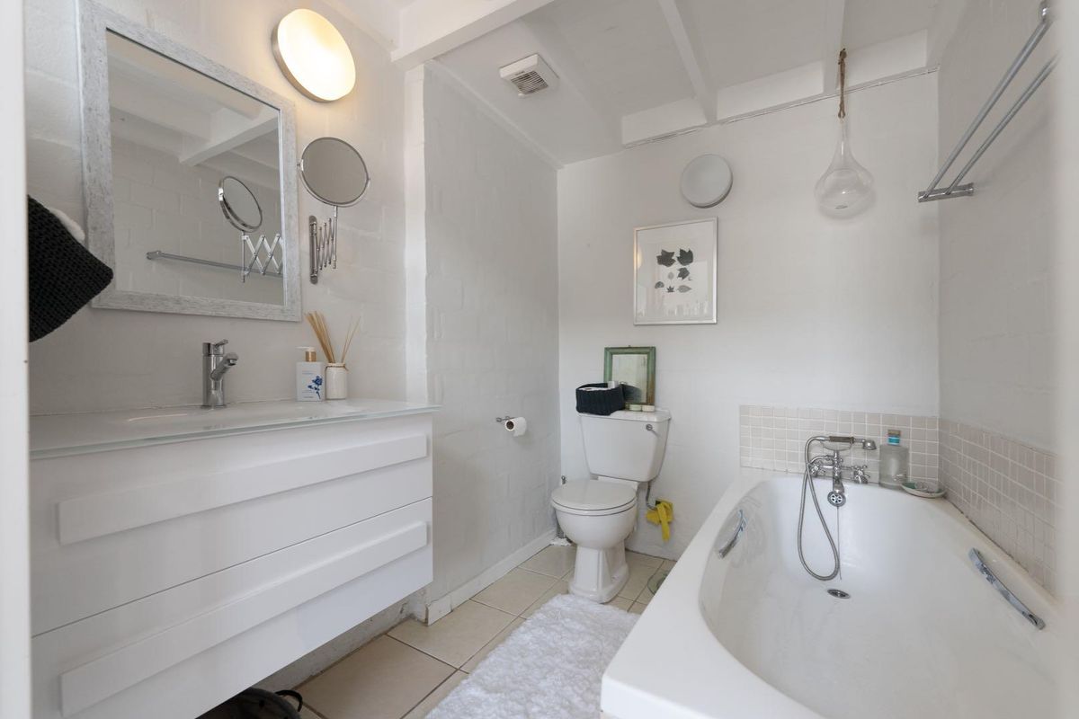 A clean and functional bathroom featuring a white vanity, a bathtub with a handheld shower attachment, and a wall-mounted mirror.