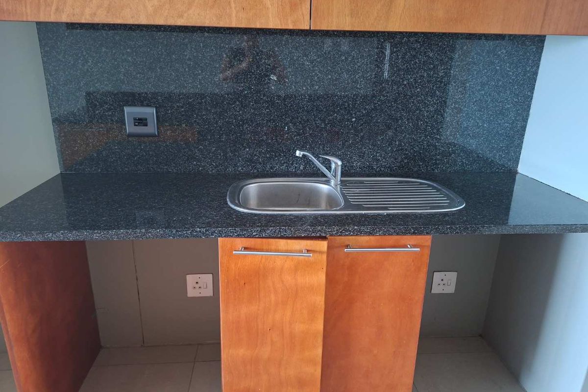 A compact kitchen area featuring dark granite countertops, a stainless steel sink, and wooden cabinetry with integrated electrical outlets.