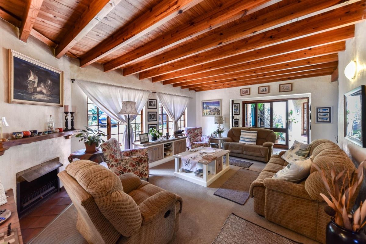 A cozy living room featuring exposed timber ceiling beams, a fireplace with a tiled hearth, and sliding glass doors leading to the exterior.