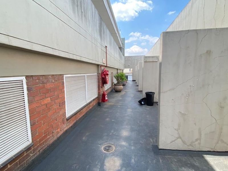 An outdoor balcony or walkway area featuring brickwork, louvre shutters, and a fire safety point, showing signs of wear on the exterior walls.