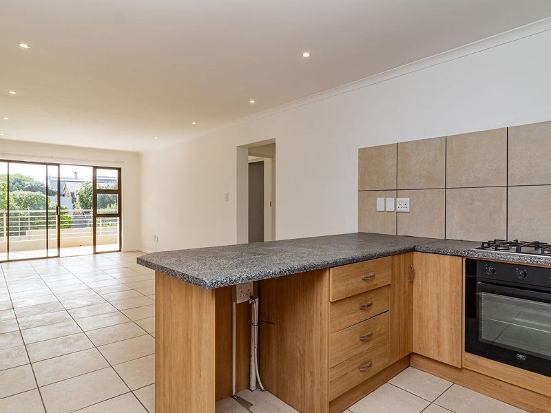 An open-plan living and kitchen area featuring tiled floors, recessed lighting, and a functional kitchen with built-in oven, gas hob, and granite countertops.