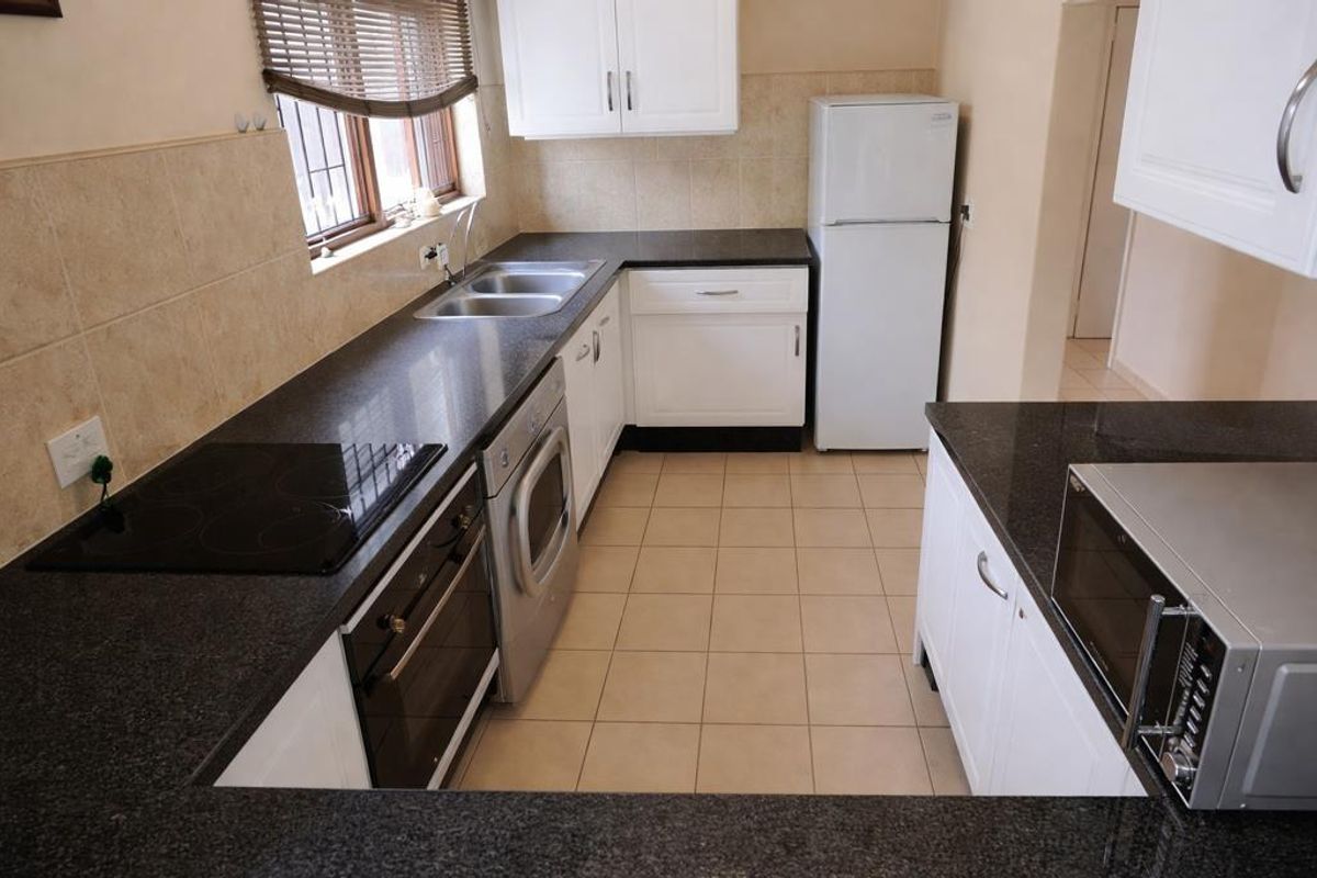 A functional kitchen featuring dark granite countertops, white cabinetry, a built-in oven, electric hob, and tiled flooring.