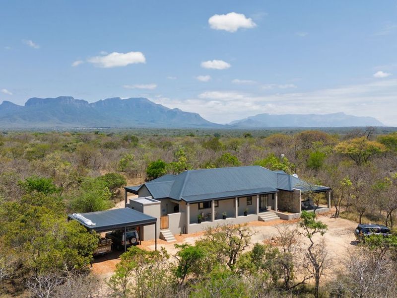 Aerial view of a modern bushveld home featuring a metal roof, stone accents, and a spacious covered patio set against a scenic mountain backdrop.