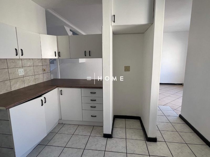 A functional kitchen area featuring white built-in cabinetry, laminate countertops, tiled backsplash, and dedicated space for a refrigerator.