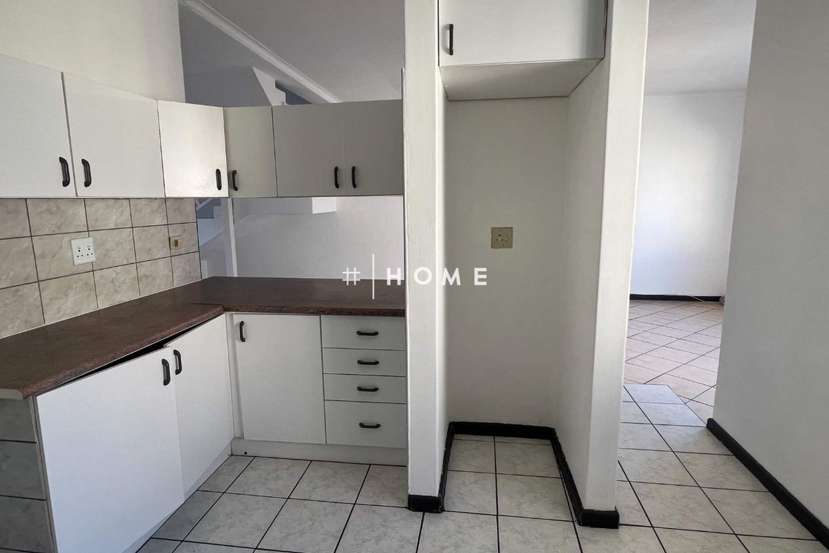 A functional kitchen area featuring white built-in cabinetry, laminate countertops, tiled backsplash, and dedicated space for a refrigerator.