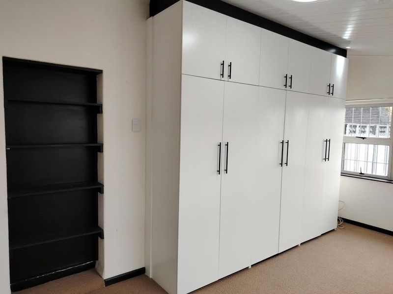 A clean bedroom featuring extensive white built-in cupboards with modern black handles and a convenient recessed shelving unit.