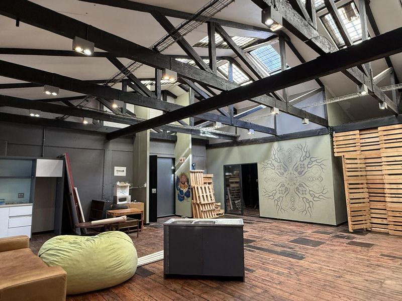 Spacious open-plan office area featuring high ceilings with exposed timber trusses, skylights, track lighting, and a functional kitchenette corner.