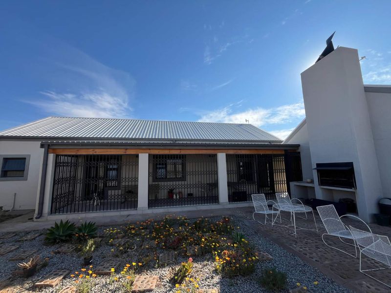 A covered patio area featuring a built-in braai, metal security gates, and a paved outdoor space overlooking a landscaped garden.