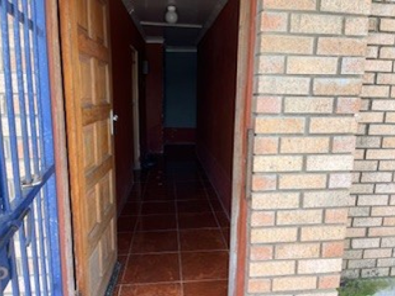 An entrance hallway featuring tiled flooring, a wooden door, and a security gate, leading into the interior of the home.