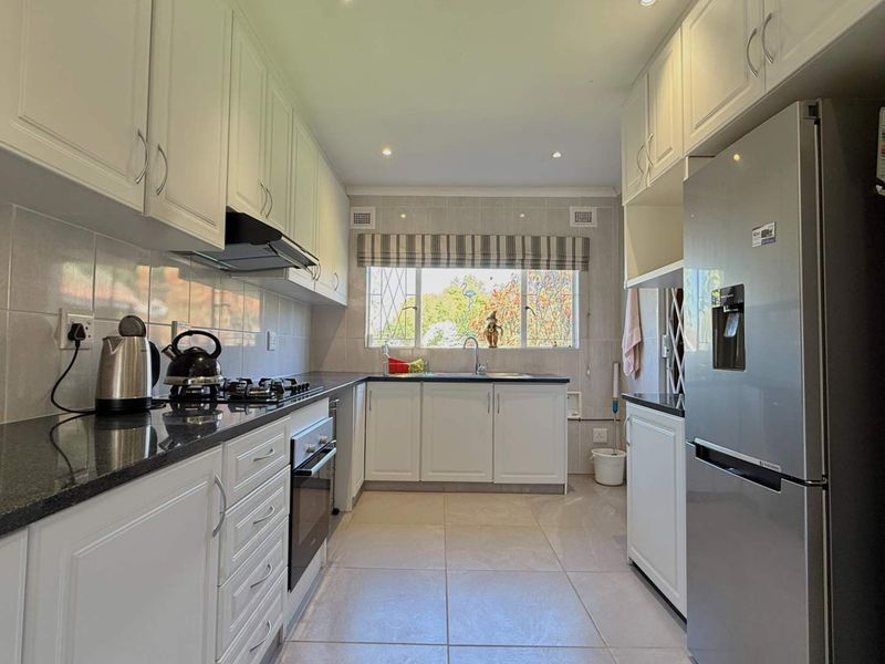 A well-maintained kitchen featuring white cabinetry, granite countertops, a gas hob, built-in oven, and tiled flooring with ample natural light.