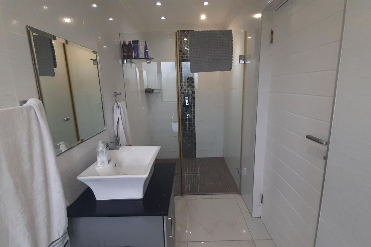 Modern bathroom featuring a vessel sink on a vanity cabinet, a glass-enclosed shower with mosaic tile accents, and polished floor tiles.