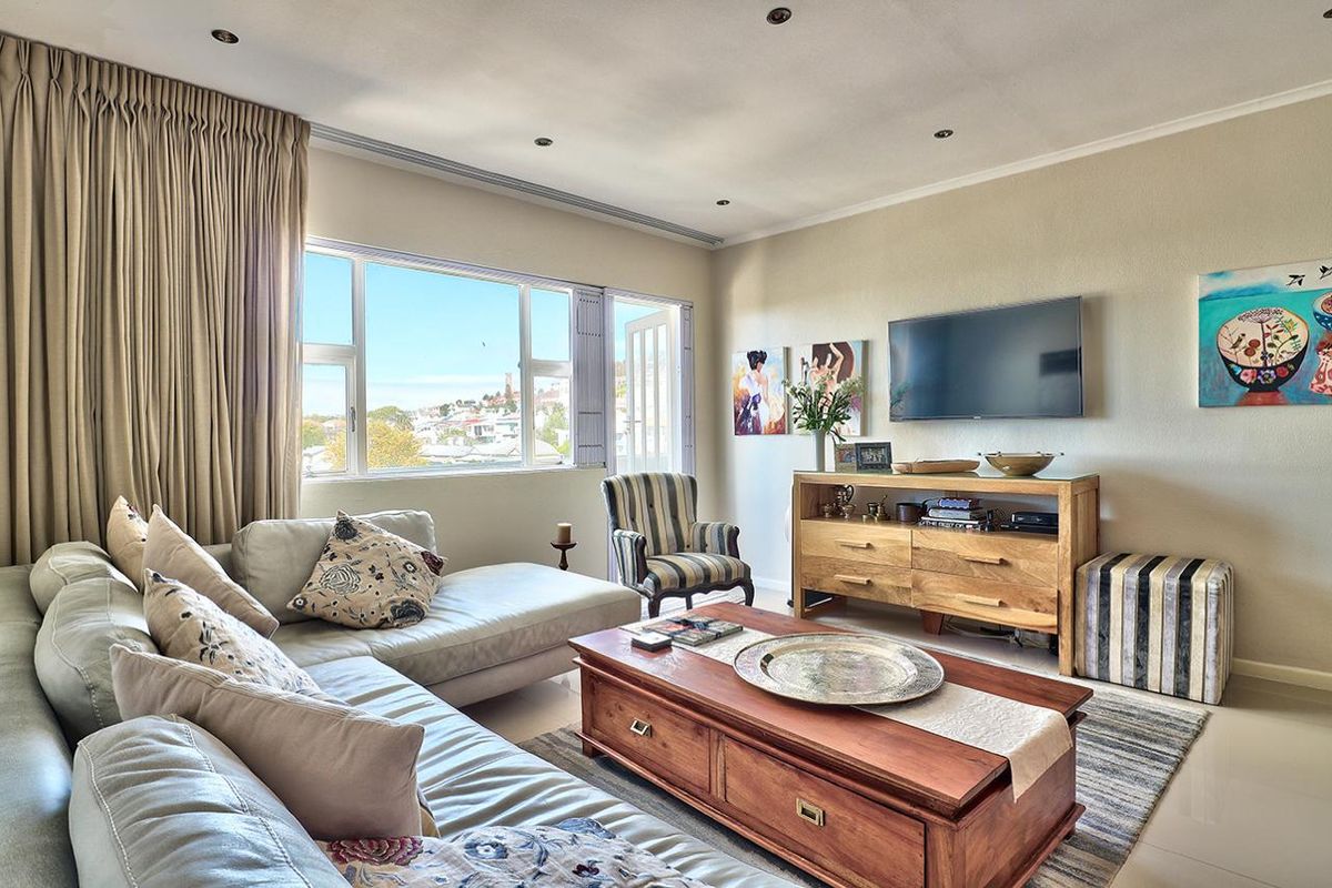 A bright and comfortable living room featuring large windows that provide natural light and views, complemented by recessed downlighting and neutral tiled flooring.