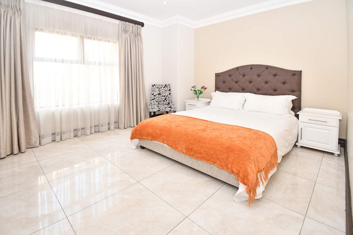 Spacious bedroom featuring large format floor tiles, neutral wall finishes, and a large window with integrated curtain tracks.