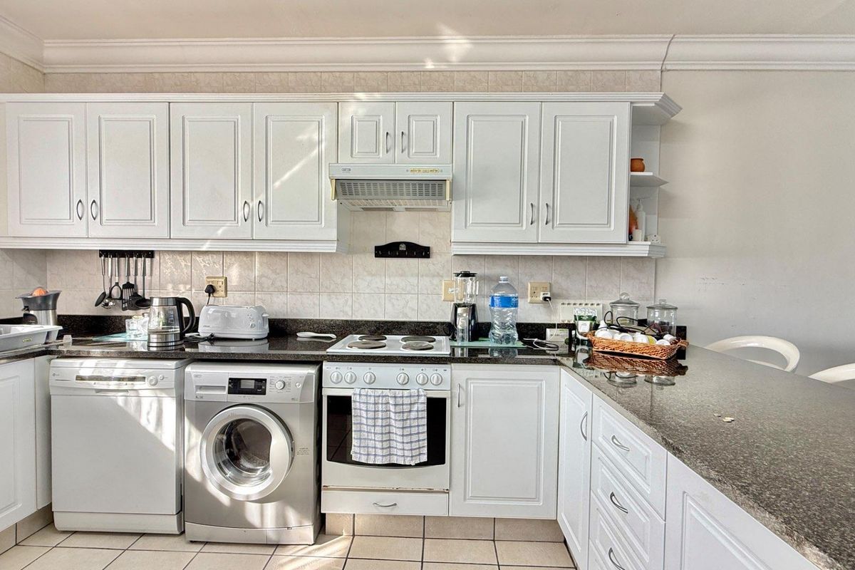 A functional kitchen featuring white cabinetry, granite countertops, tiled backsplash, and integrated appliances including an oven, hob, and extractor fan.