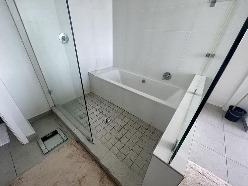 A bathroom featuring a combined shower and bathtub area with glass enclosure, tiled flooring, and wall-mounted chrome fixtures.