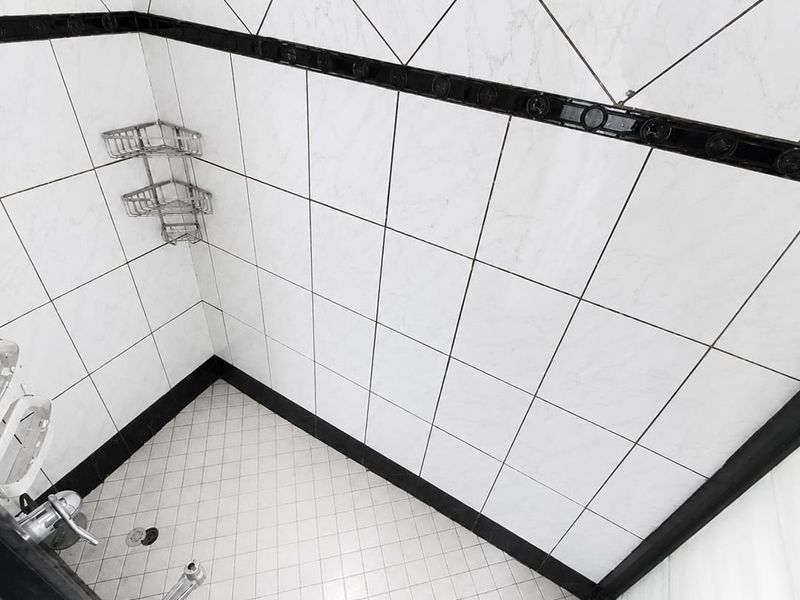 A clean shower enclosure featuring white tiled walls with a decorative black border and matching tiled flooring.