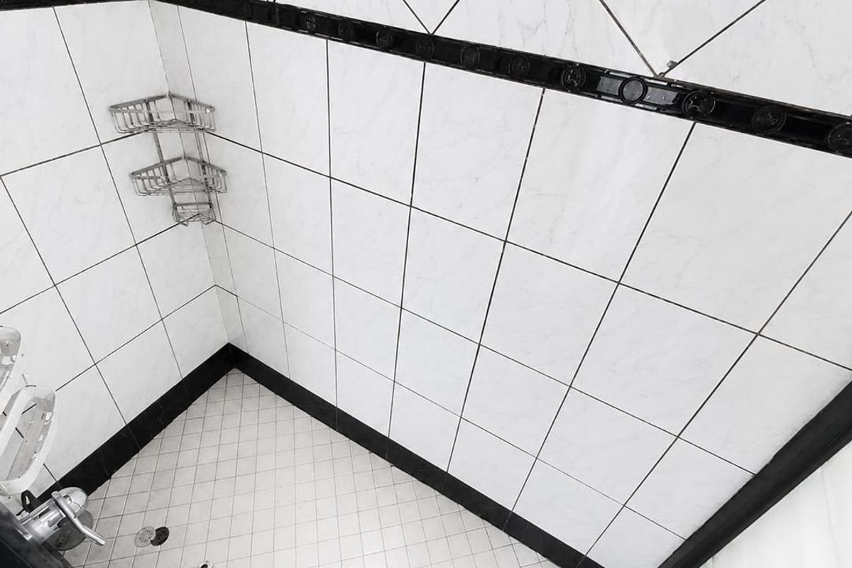 A clean shower enclosure featuring white tiled walls with a decorative black border and matching tiled flooring.