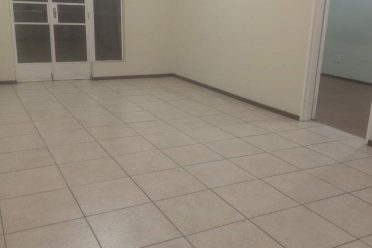 An empty living area featuring neutral ceramic floor tiles and a glass-paneled door leading to an outdoor space.