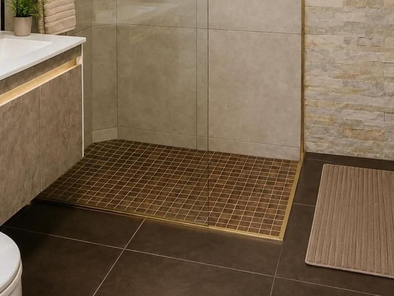 Modern bathroom featuring a walk-in shower with glass screen, stone feature wall, vanity with brass fixtures, and dark floor tiling.