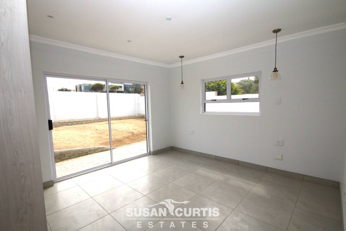 A bright, modern living area featuring large sliding glass doors, neutral floor tiles, and contemporary pendant lighting, offering direct access to the rear garden.