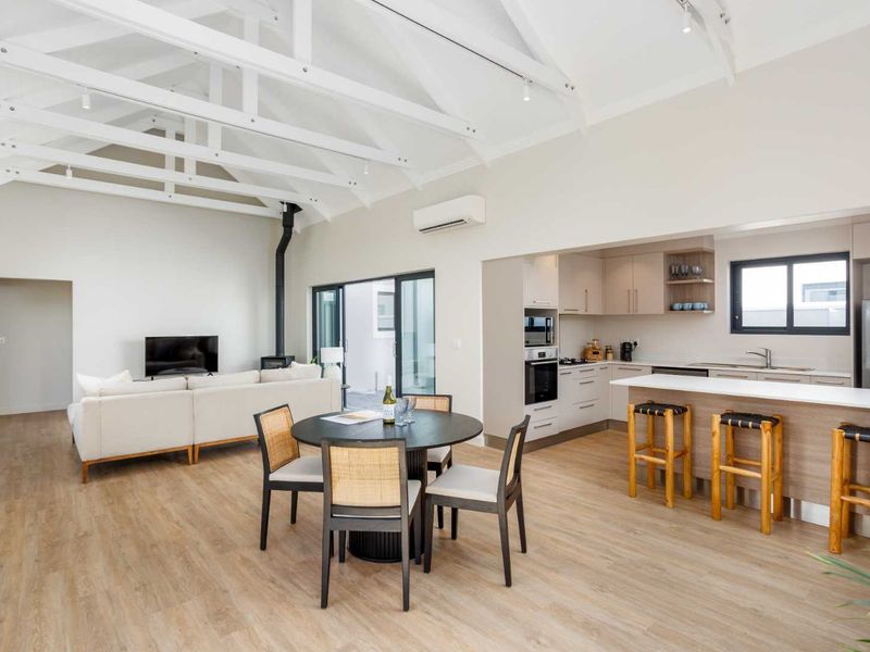 Spacious open-plan living area featuring high vaulted ceilings with exposed trusses, a modern kitchen with island, and seamless flow to the outdoor patio.