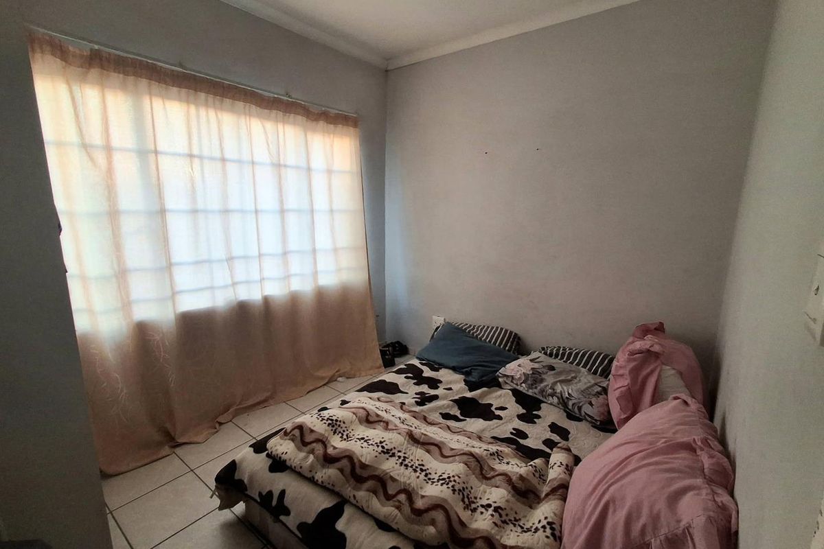 A standard bedroom featuring tiled flooring and a large window with curtain rails, providing a functional space for rest.