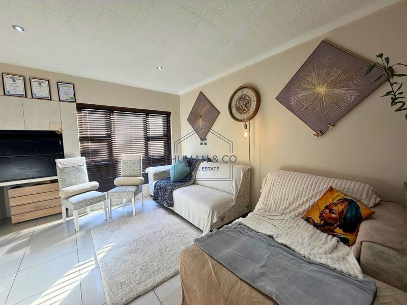 A comfortable living room featuring tiled flooring, recessed downlighting, and a built-in media unit, complemented by large windows with venetian blinds.