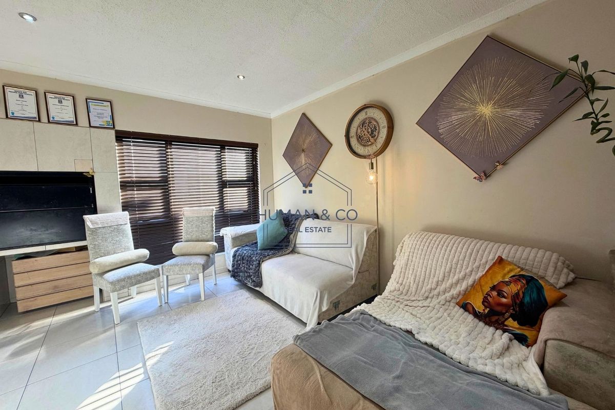 A comfortable living room featuring tiled flooring, recessed downlighting, and a built-in media unit, complemented by large windows with venetian blinds.