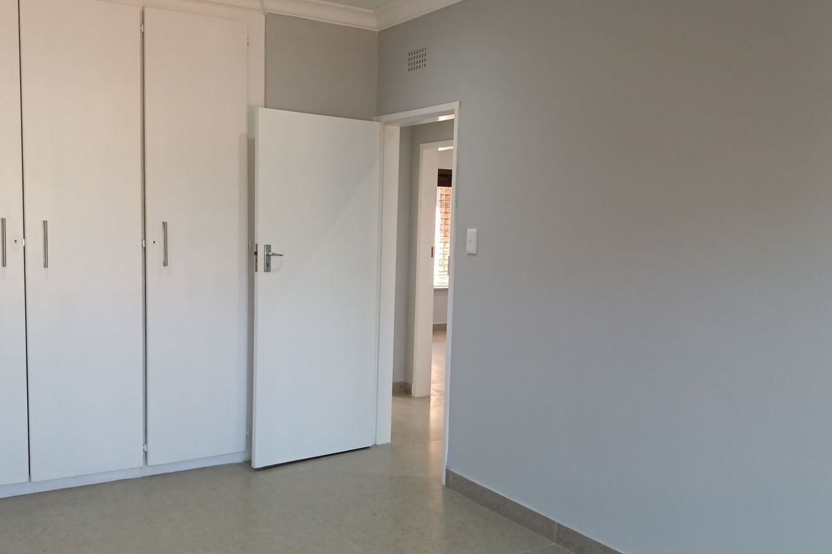 A clean, empty bedroom featuring neutral walls, tiled flooring, and built-in cupboards, offering a versatile space ready for personalization.