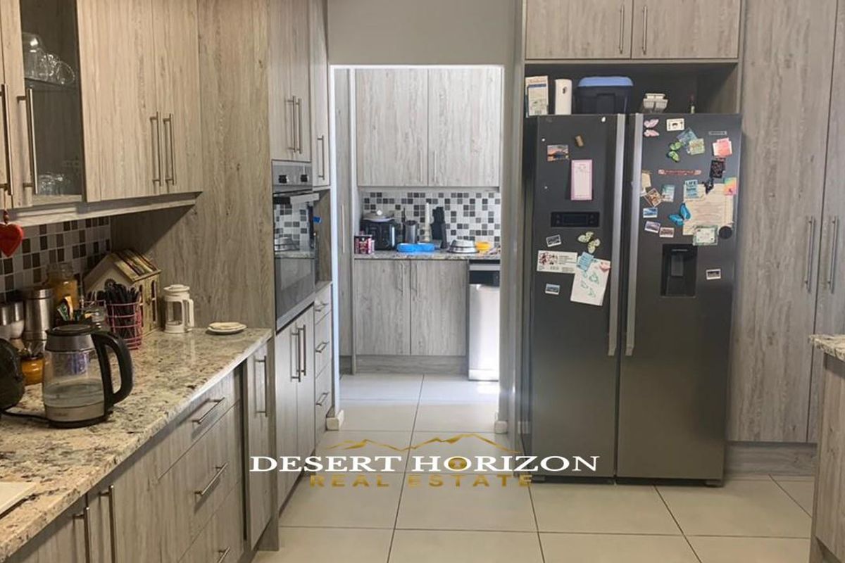 A functional kitchen featuring wood-grain cabinetry, granite countertops, and a tiled backsplash, with an adjoining scullery area for additional prep and storage.