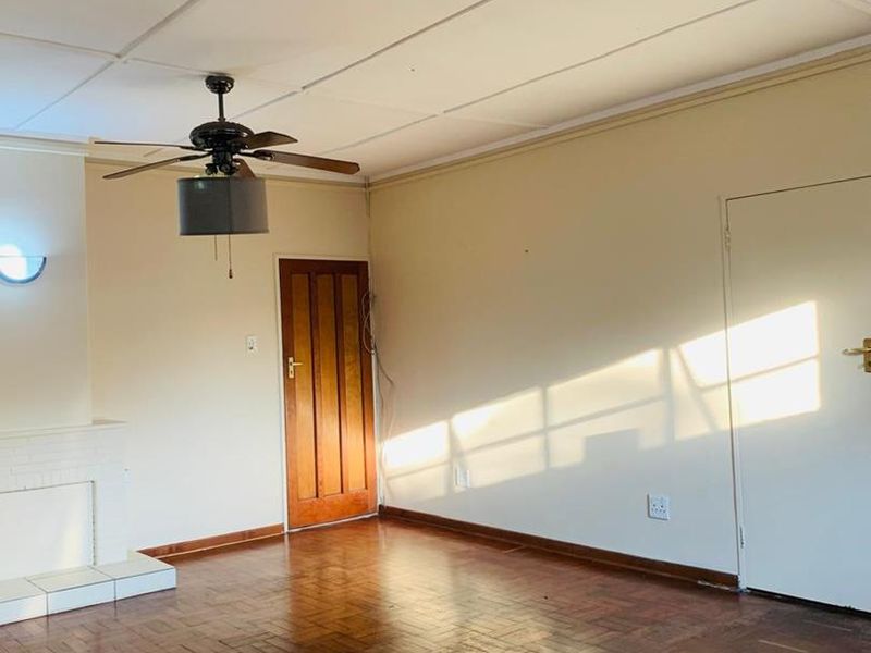 Spacious living room featuring original parquet flooring, a ceiling fan, and a fireplace hearth, offering a blank canvas for interior design.