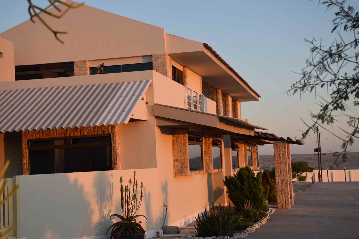 A side view of a multi-level residential building featuring stone cladding accents, large windows, and a covered patio area at sunset.
