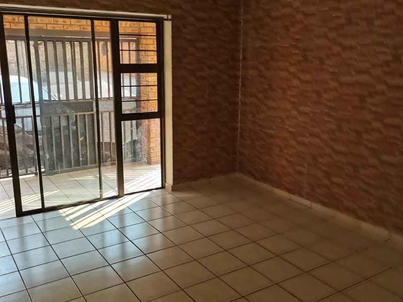 An empty living room featuring tiled flooring, textured wall finishes, and a sliding glass door leading to an outdoor area with security gates.