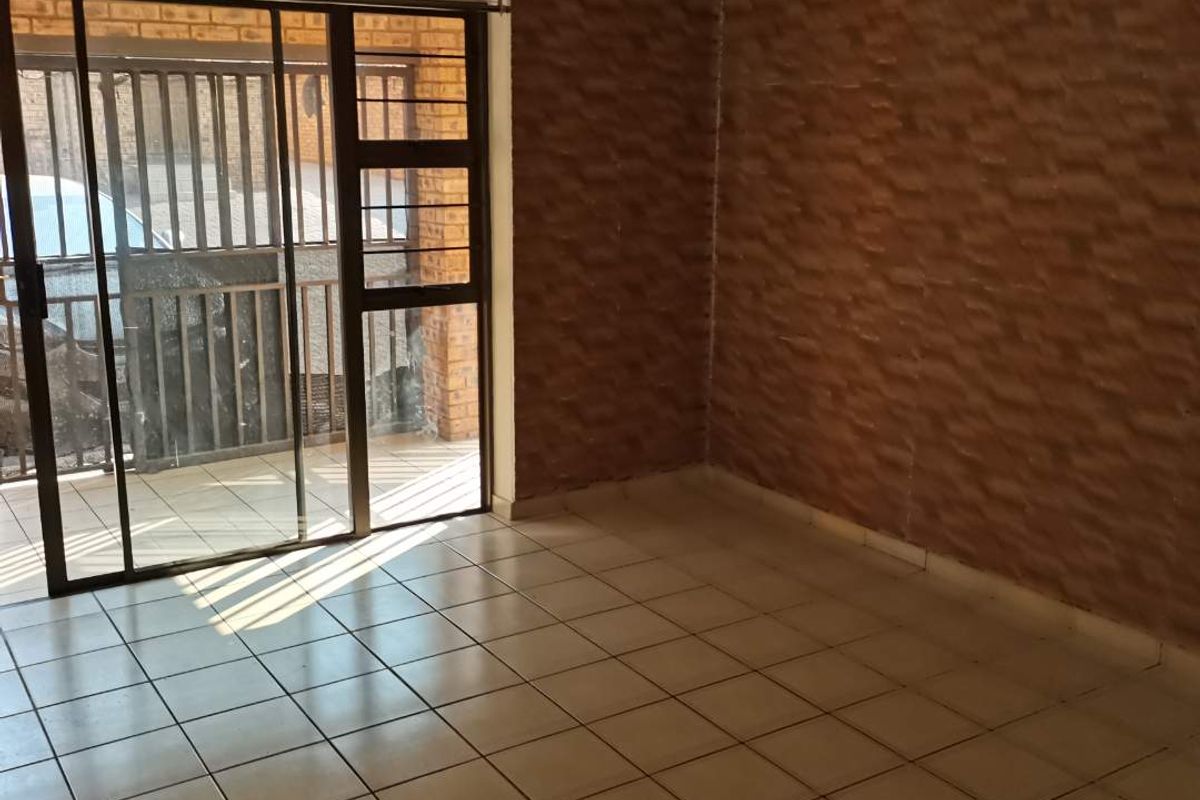 An empty living room featuring tiled flooring, textured wall finishes, and a sliding glass door leading to an outdoor area with security gates.