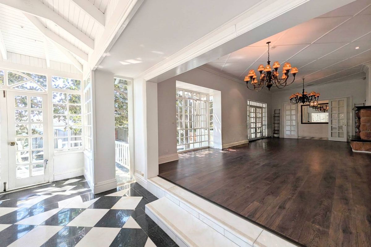 Spacious living area featuring vaulted ceilings, dark timber flooring, a stone fireplace, and elegant french doors leading to outdoor spaces.