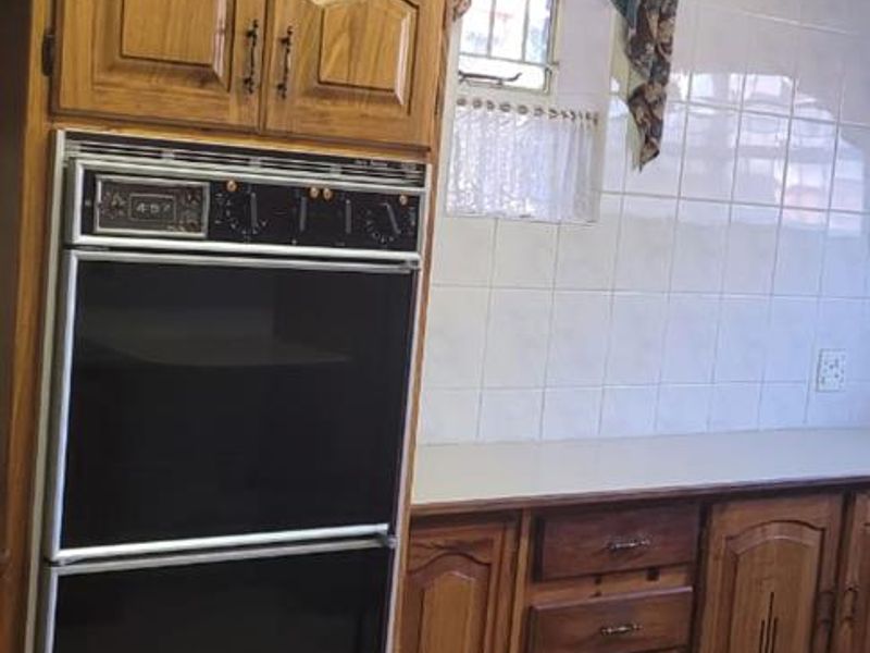 A functional kitchen featuring traditional wooden cabinetry, a built-in double oven, tiled splashbacks, and ceramic floor tiles.